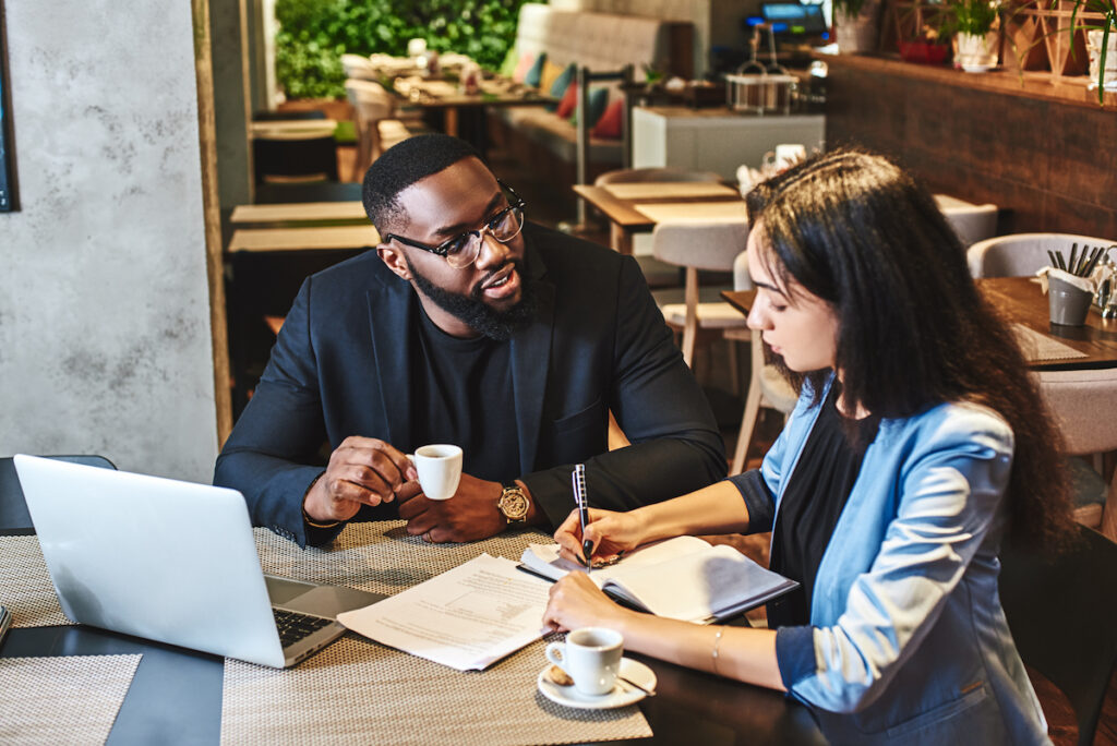 Two business professionals engaged in a discussion in a coffee shop setting.